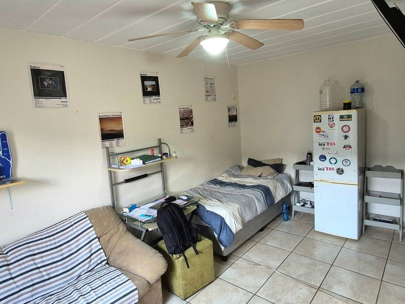 A functional bedroom featuring tiled flooring, a ceiling fan, and wall-mounted shelving, providing a practical living space.
