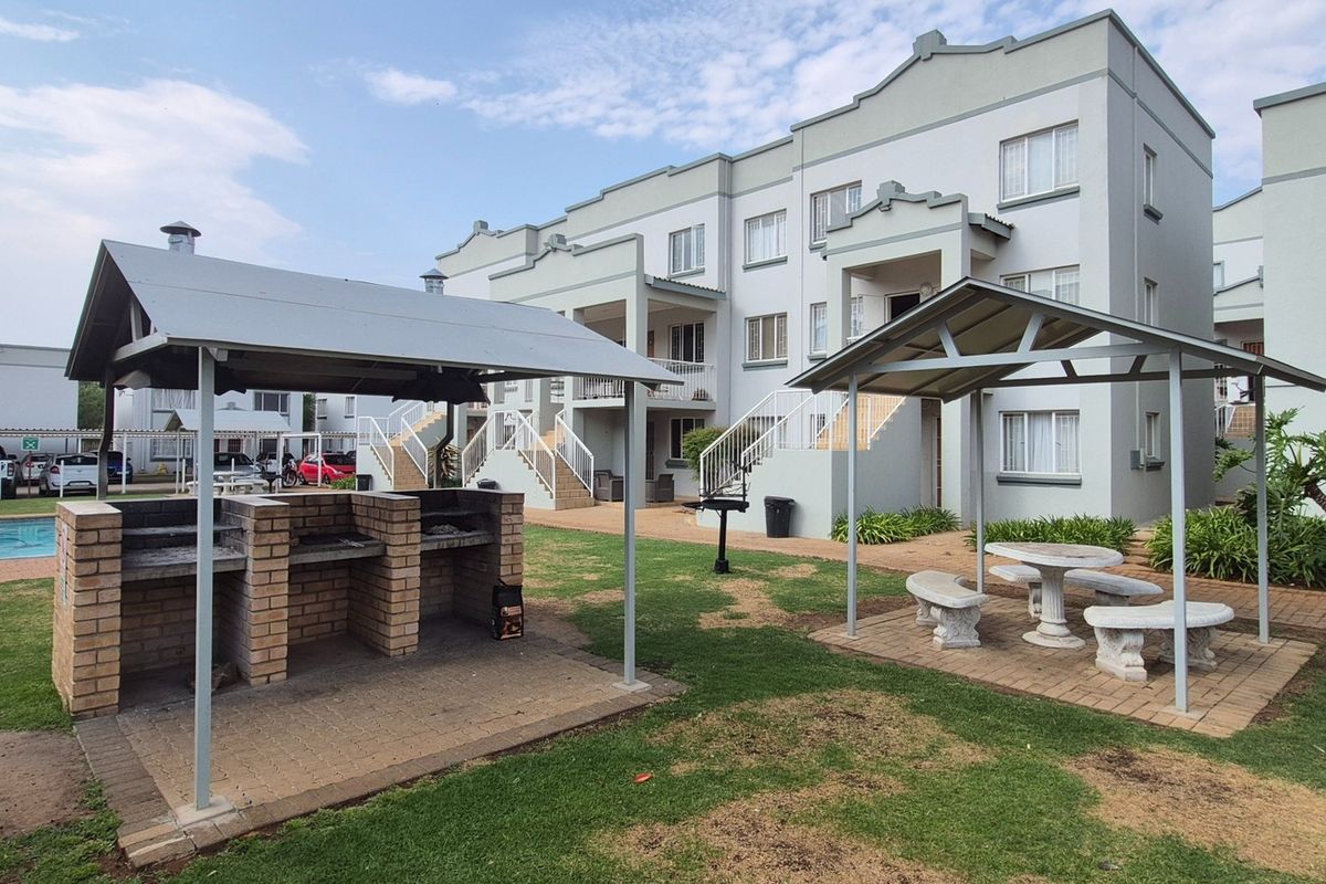 Communal outdoor area featuring a brick braai facility, covered seating, and a swimming pool set within the apartment complex grounds.