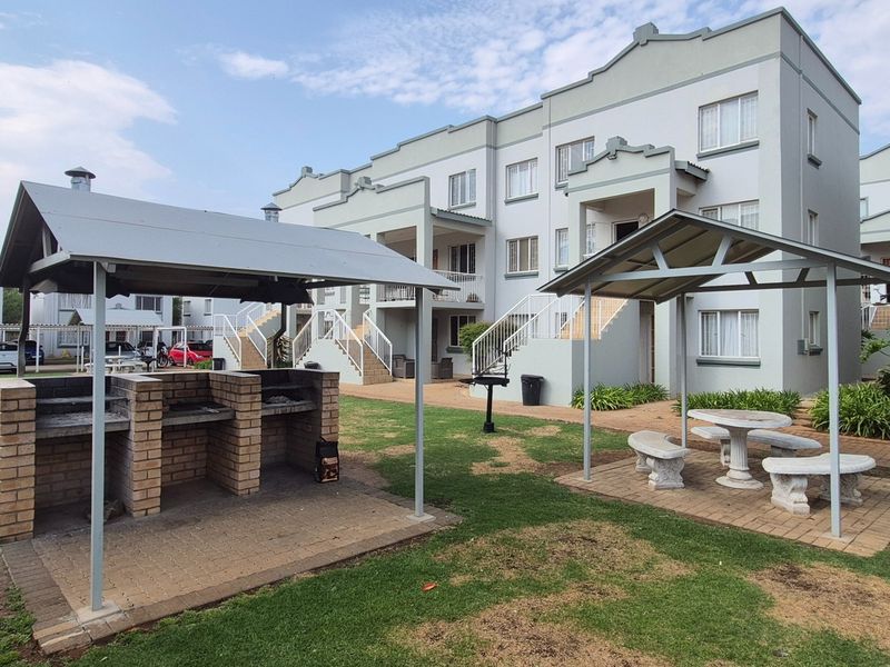 Communal outdoor area featuring a brick braai facility, covered seating, and a swimming pool set within the apartment complex grounds.