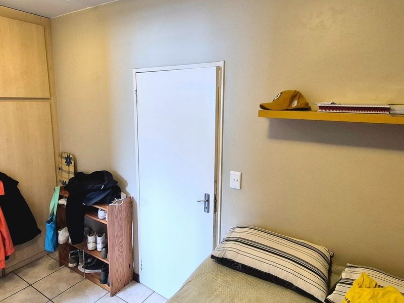 A functional bedroom featuring built-in cupboards, tiled flooring, and a floating wall shelf, offering practical storage and living space.