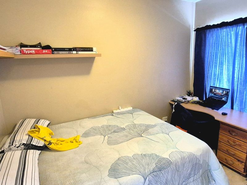 A functional bedroom featuring a floating wall shelf and a window with blue curtains, providing a comfortable space for rest and study.