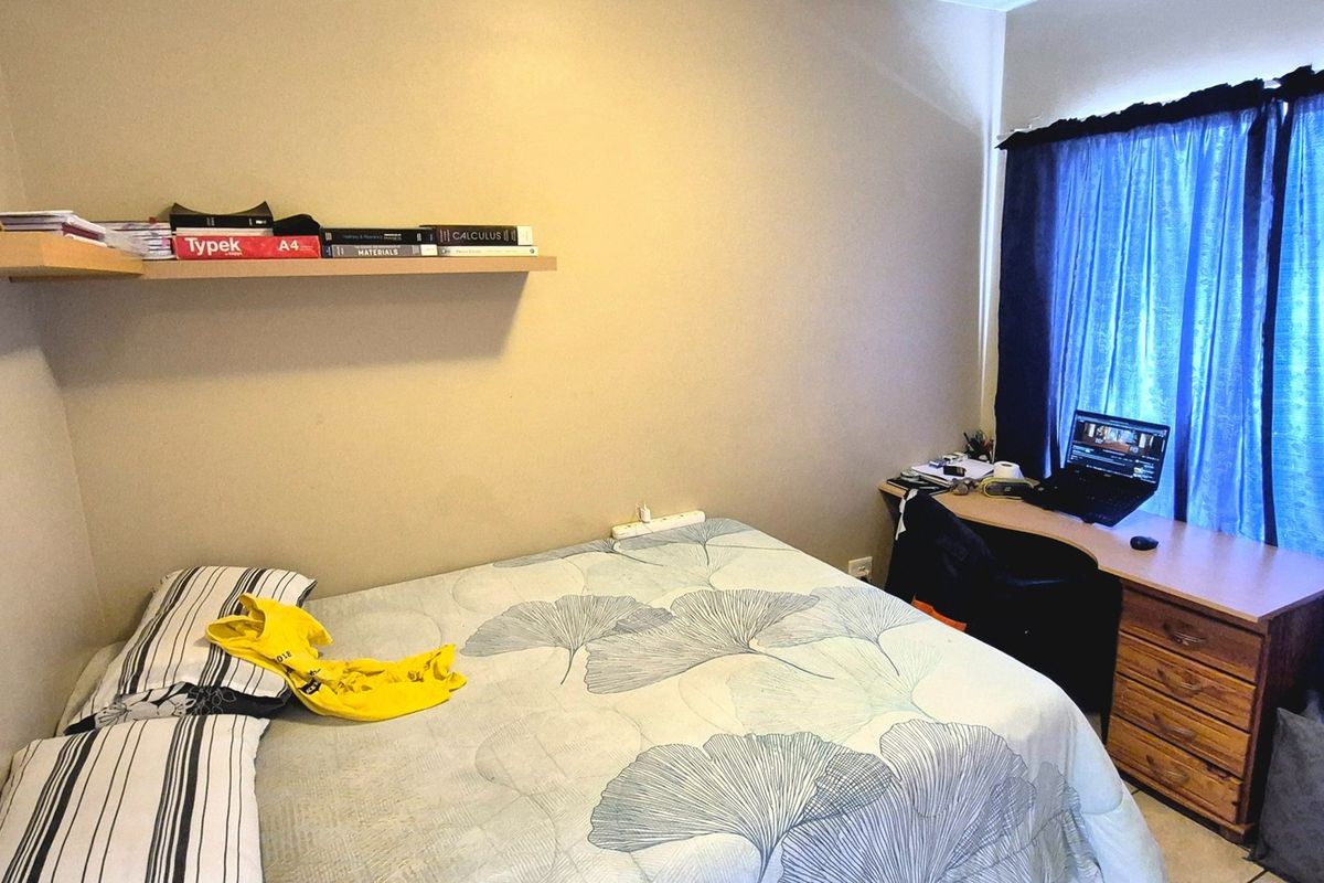 A functional bedroom featuring a floating wall shelf and a window with blue curtains, providing a comfortable space for rest and study.