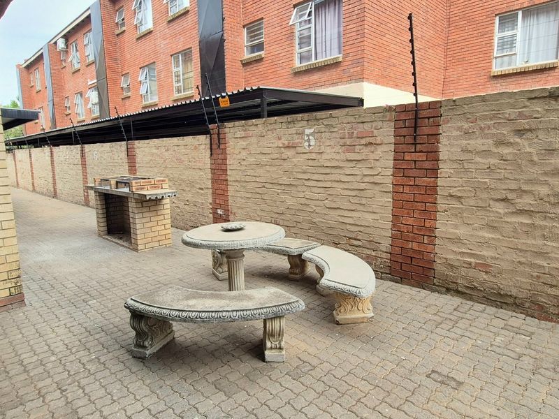 Outdoor patio area featuring paved flooring, a built-in brick braai, and a high boundary wall with electric fencing.