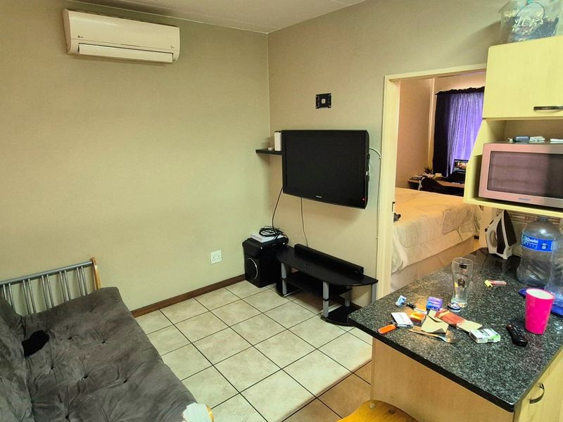 Open-plan living area featuring tiled floors, a compact kitchen with built-in cabinetry, and a wall-mounted air conditioning unit.