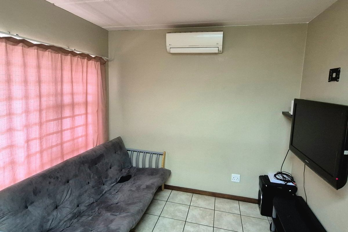 A functional living room featuring tiled flooring, a wall-mounted air conditioning unit, and a large window with curtains.