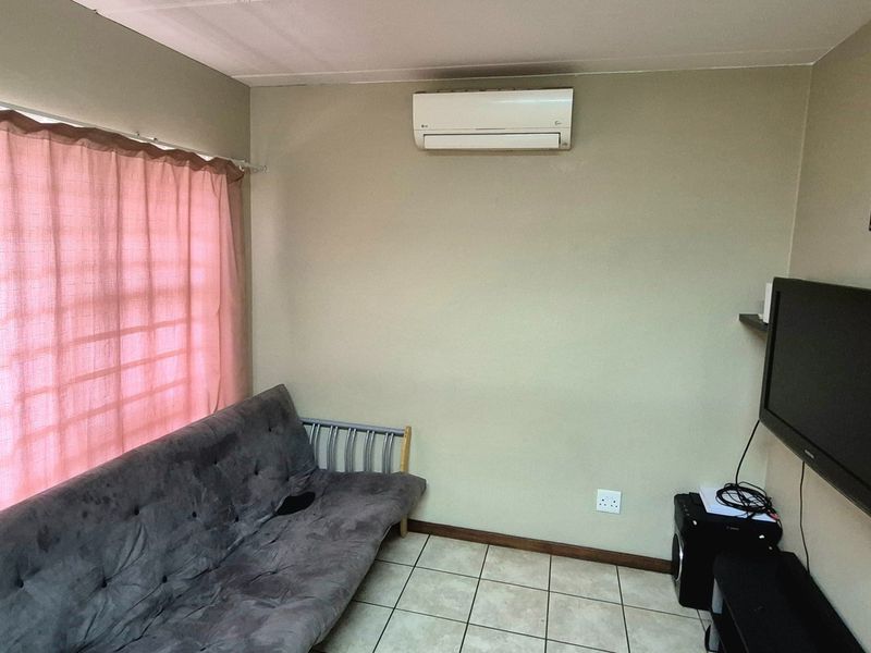 A functional living room featuring tiled flooring, a wall-mounted air conditioning unit, and a large window with curtains.