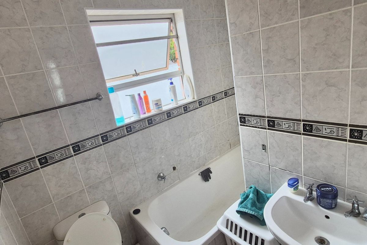 A functional bathroom featuring a bathtub, pedestal basin, toilet, and tiled walls with decorative border accents.