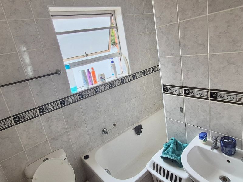 A functional bathroom featuring a bathtub, pedestal basin, toilet, and tiled walls with decorative border accents.