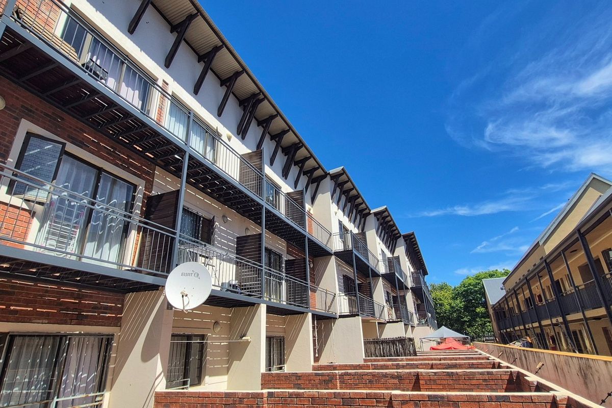 Exterior view of a multi-story apartment complex featuring brick and plaster facades, metal balconies, and external access staircases.