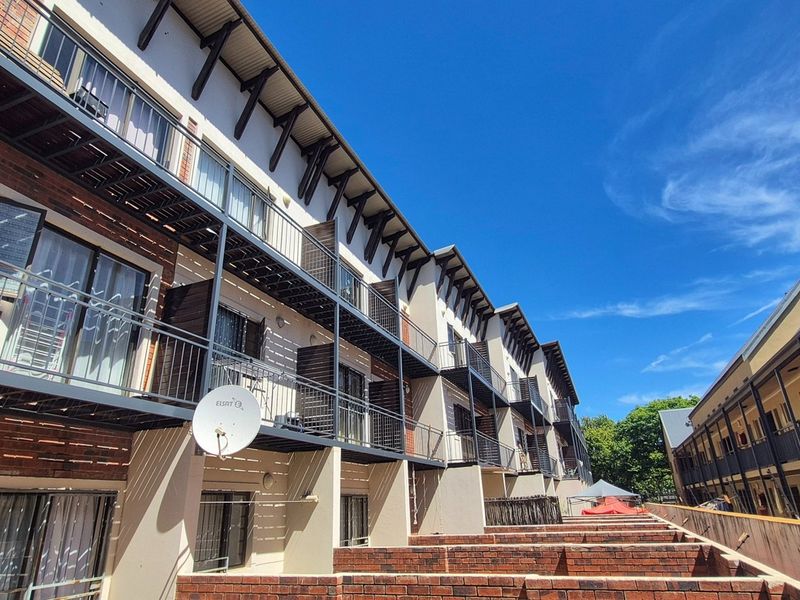 Exterior view of a multi-story apartment complex featuring brick and plaster facades, metal balconies, and external access staircases.