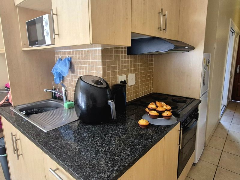 Compact kitchen featuring light wood cabinetry, granite countertops, tiled backsplash, and integrated appliances including an oven, hob, and extractor fan.