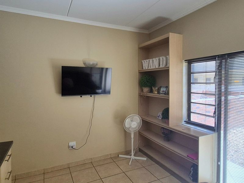 Open plan living area featuring tiled floors, built-in cabinetry, a fixed shelving unit, and a sliding door with security bars leading to the exterior.