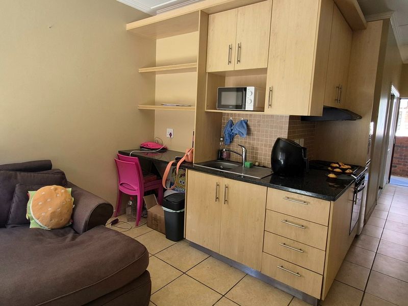 Compact open-plan living area featuring a kitchenette with built-in cabinetry, integrated oven, extractor fan, and tiled flooring throughout.