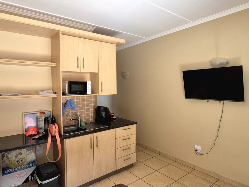 A compact kitchenette featuring light wood cabinetry, granite countertops, a stainless steel sink, and tiled flooring, suitable for a studio or apartment living space.
