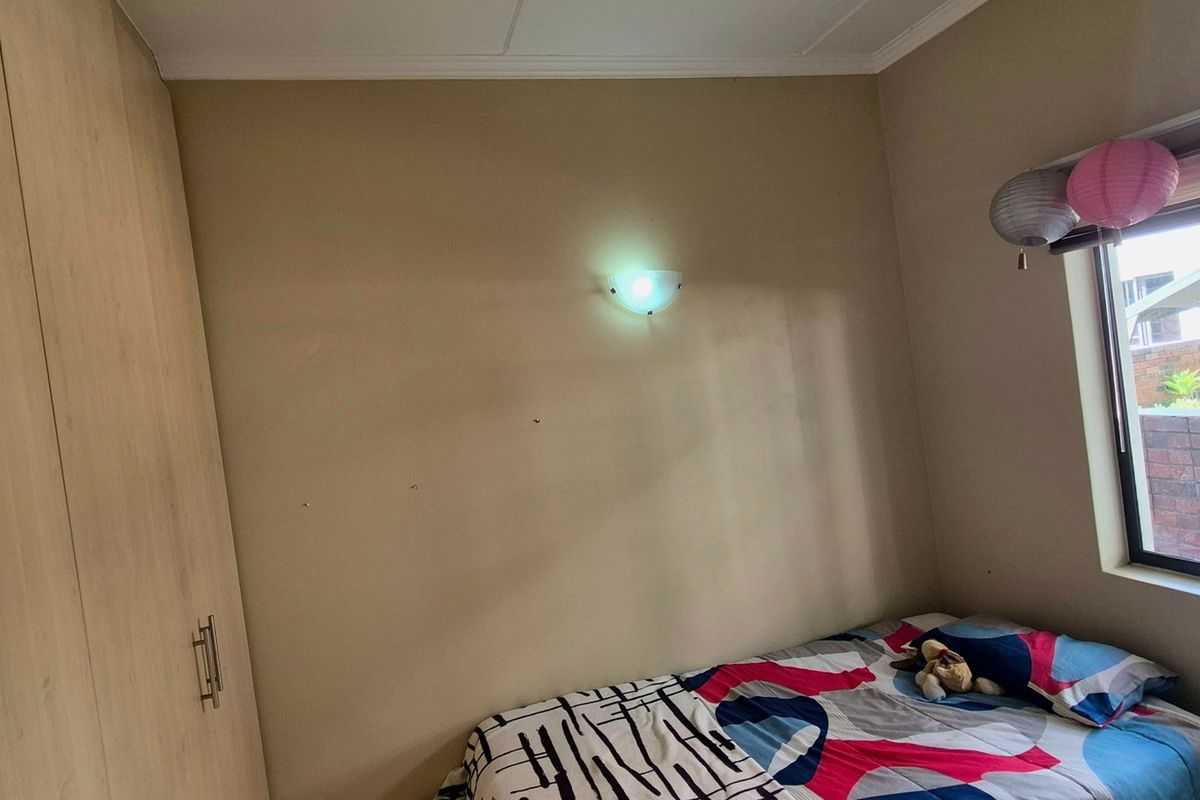 A bedroom featuring a built-in wardrobe, a wall-mounted light fixture, and a window overlooking an exterior brick wall.