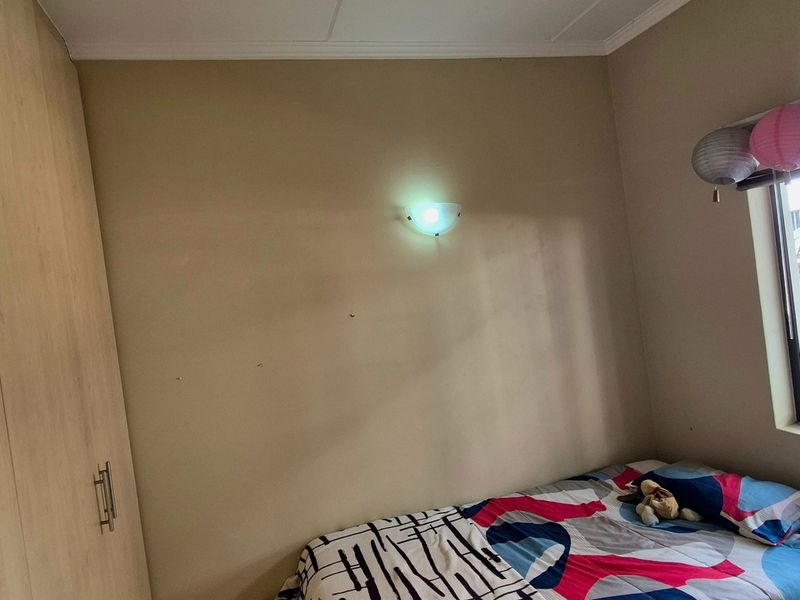 A bedroom featuring a built-in wardrobe, a wall-mounted light fixture, and a window overlooking an exterior brick wall.