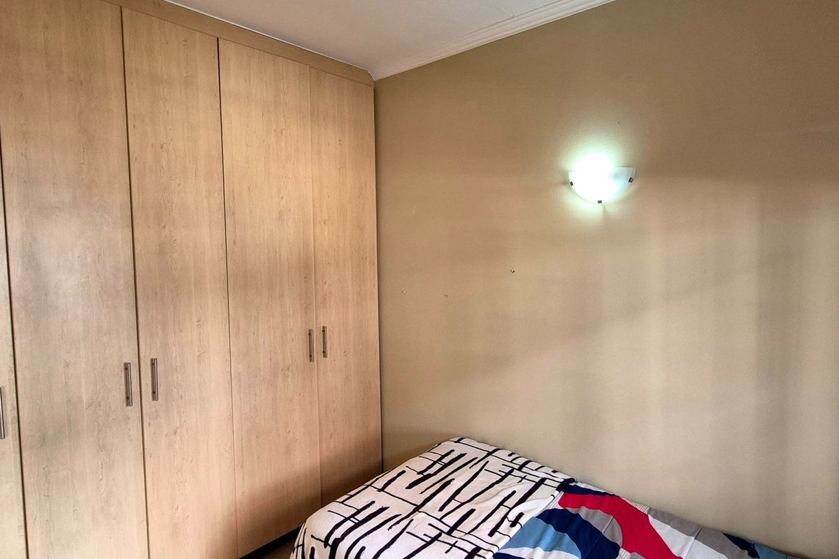 A bedroom featuring light wood-finish built-in cupboards and a wall-mounted light fixture.