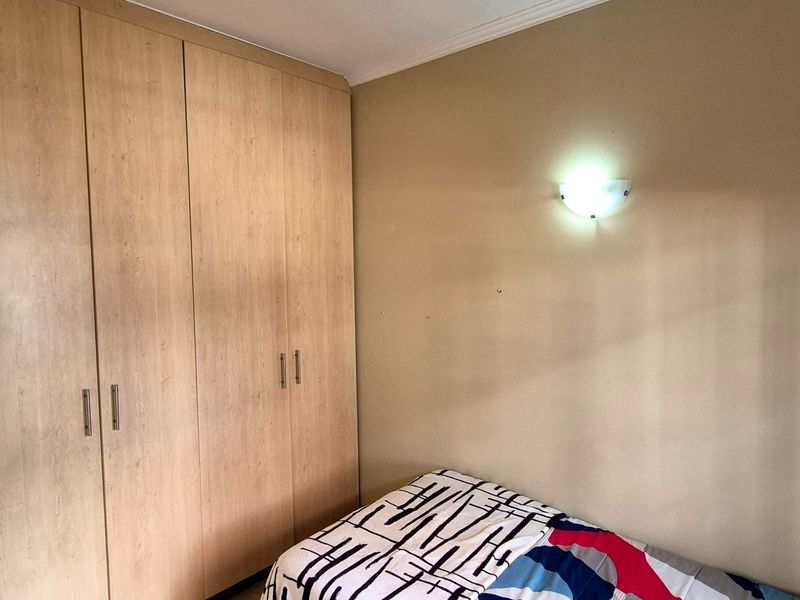 A bedroom featuring light wood-finish built-in cupboards and a wall-mounted light fixture.