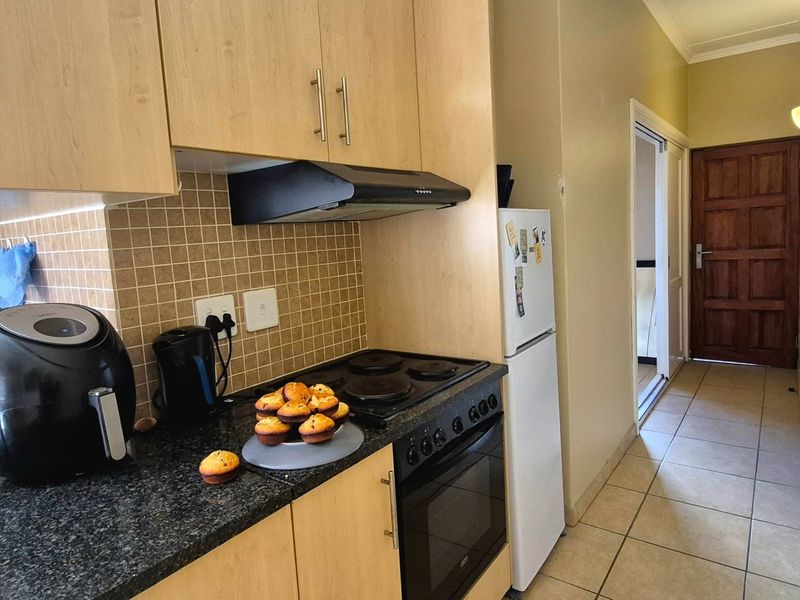 Compact kitchen featuring light wood cabinetry, dark laminate countertops, tiled backsplash, and integrated electric stove and oven.