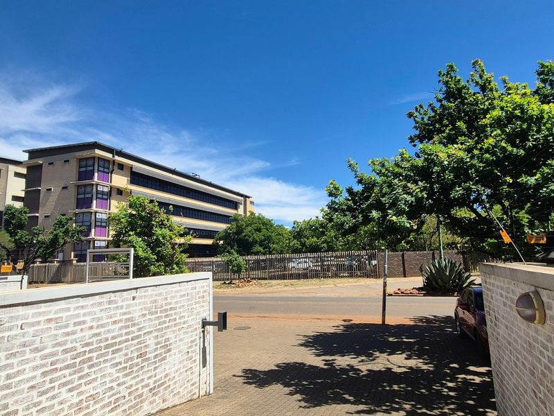 A view from the property entrance showing the paved driveway, brick boundary walls with electric fencing, and the surrounding neighbourhood street.