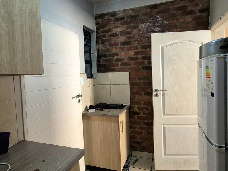 Compact kitchen featuring built-in cabinetry, laminate countertops, a tiled splashback, and a distinctive exposed brick feature wall.