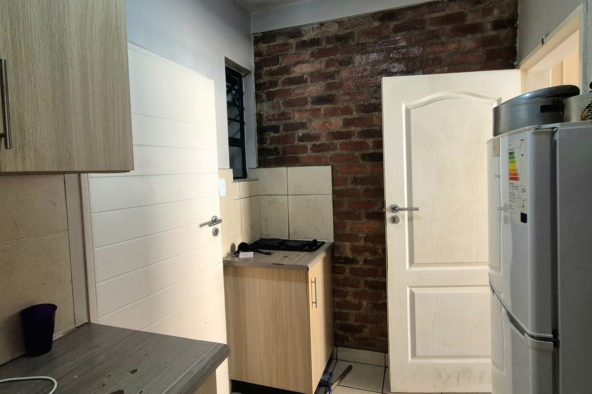 Compact kitchen featuring built-in cabinetry, laminate countertops, a tiled splashback, and a distinctive exposed brick feature wall.