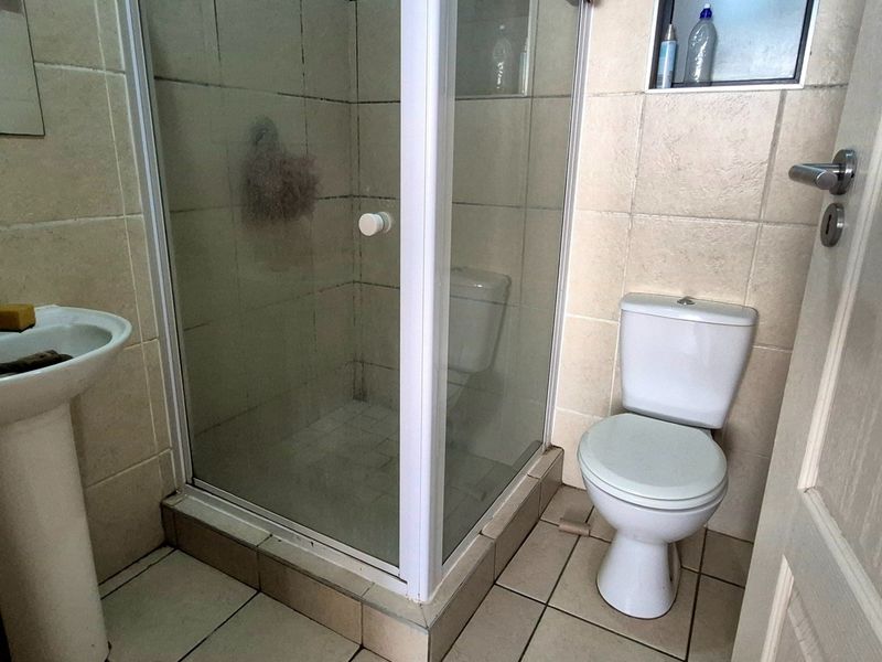 Compact bathroom featuring a pedestal basin, a shower enclosure, and a toilet with neutral wall and floor tiling.