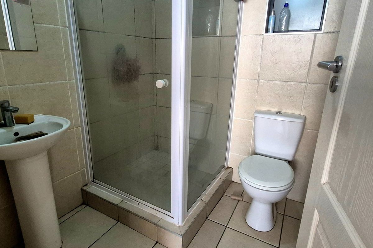 Compact bathroom featuring a pedestal basin, a shower enclosure, and a toilet with neutral wall and floor tiling.