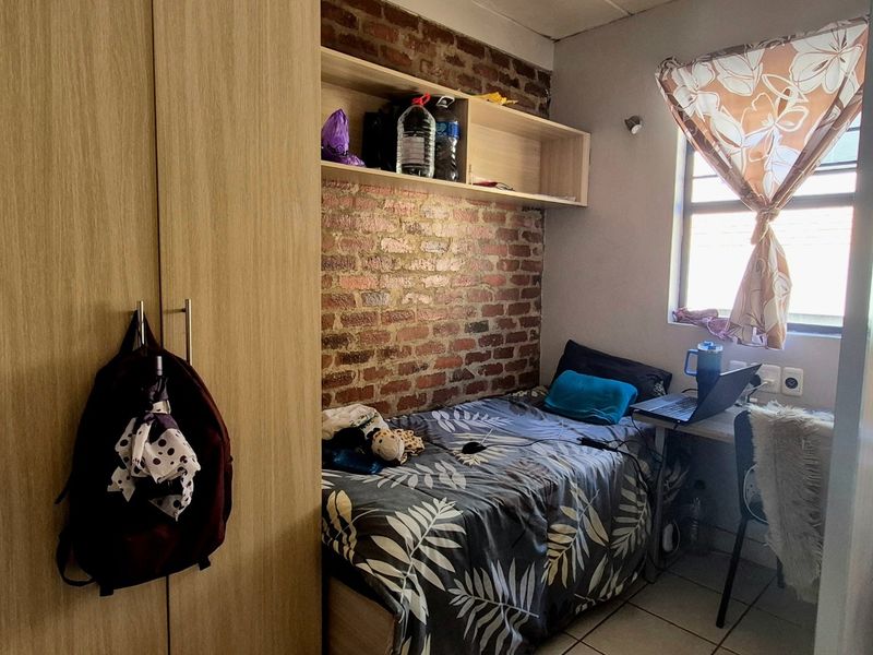 A compact bedroom featuring an exposed brick accent wall, built-in wardrobe, and tiled flooring, offering a functional living space.
