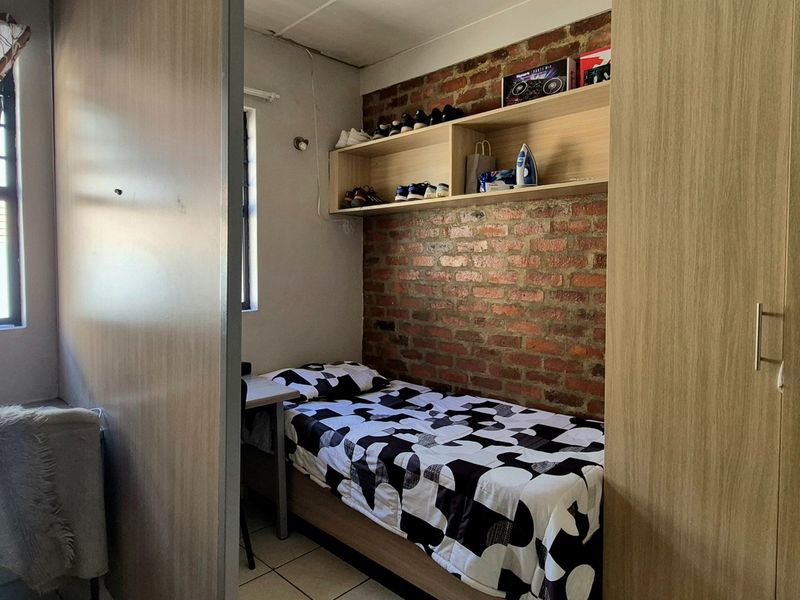 Compact bedroom featuring an exposed brick feature wall, built-in shelving, and a built-in wardrobe with tiled flooring.