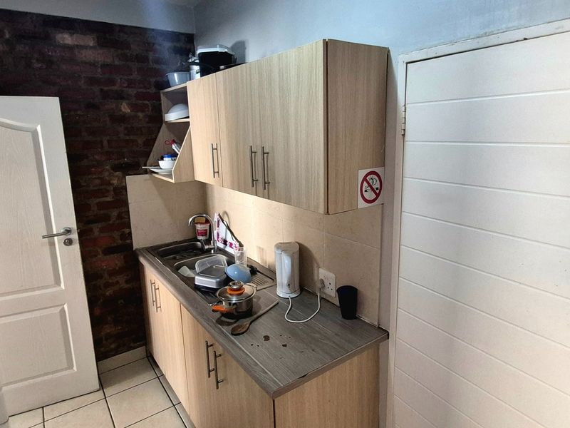 Compact kitchen featuring light wood-finish cabinetry, a stainless steel sink, and an exposed brick feature wall.