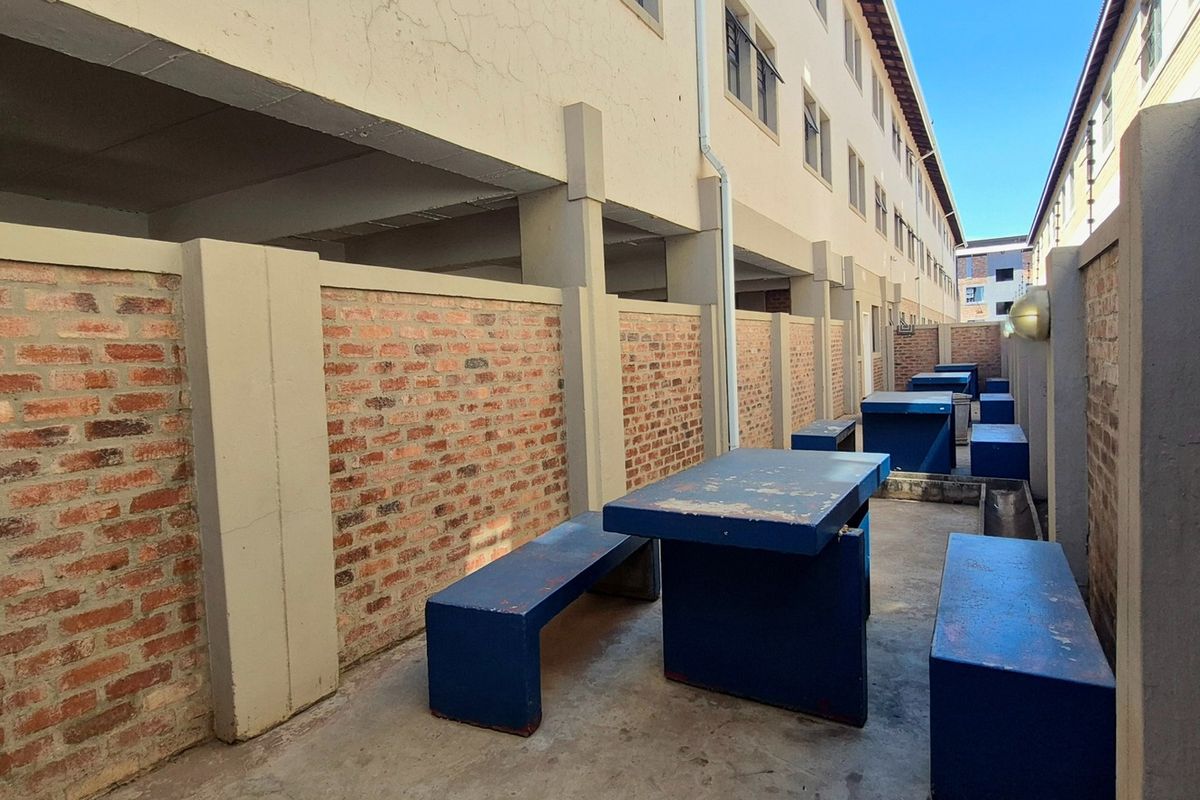 A narrow outdoor courtyard area featuring exposed brick boundary walls and concrete paving, situated between apartment building blocks.