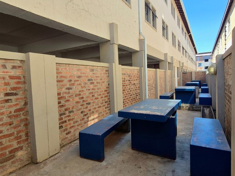 A narrow outdoor courtyard area featuring exposed brick boundary walls and concrete paving, situated between apartment building blocks.