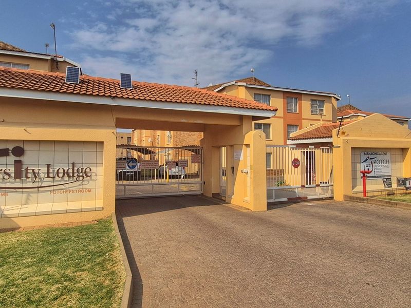 Front entrance view of Varsity Lodge apartment complex featuring secure gated access, perimeter walling with electric fencing, and paved driveway.