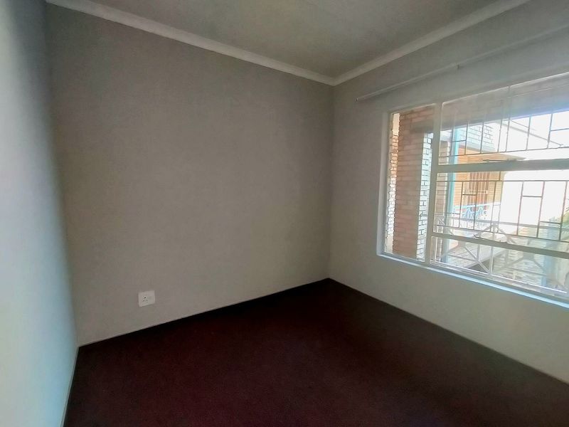 An empty bedroom featuring carpeted flooring, a window with security bars, and neutral wall finishes.