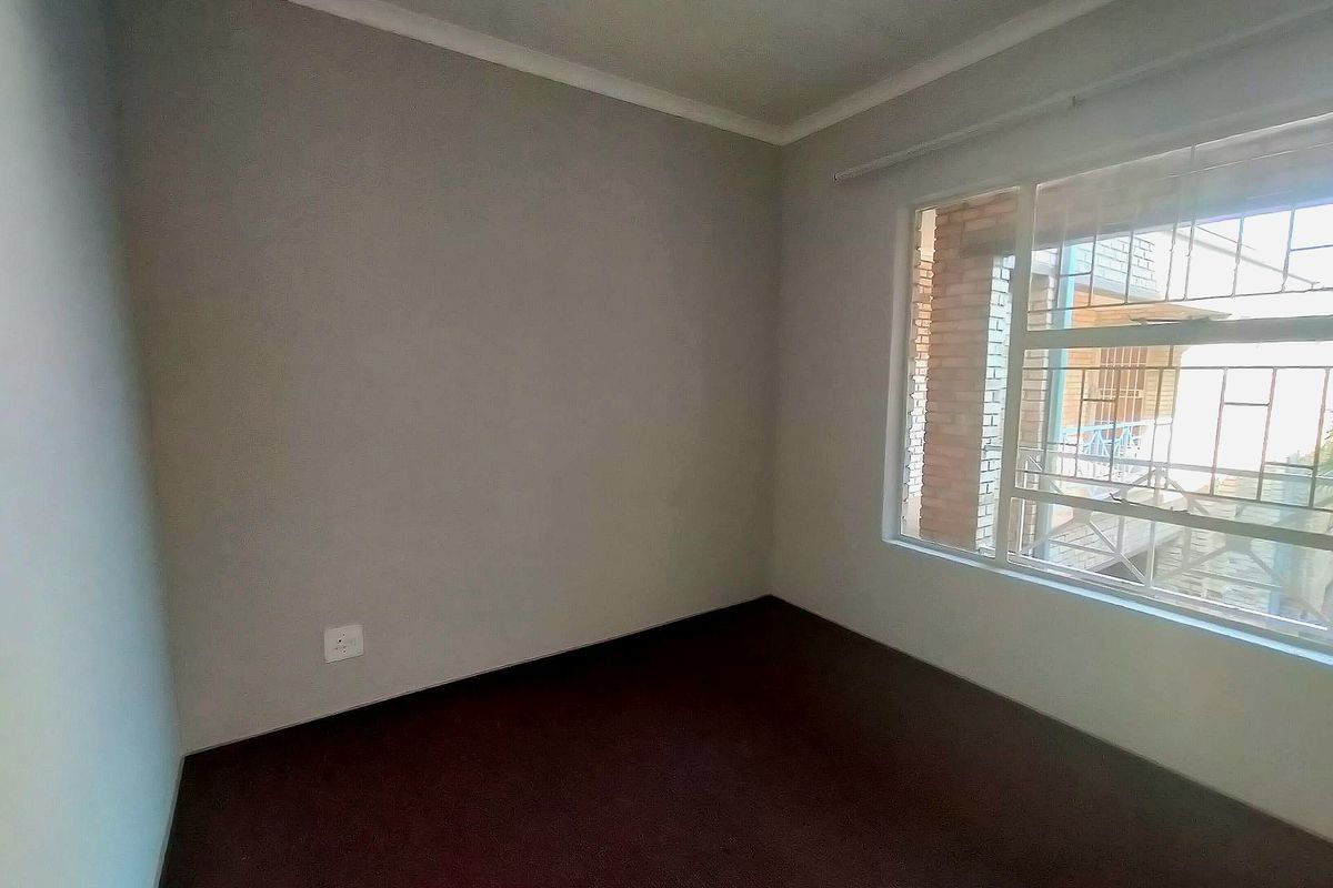 An empty bedroom featuring carpeted flooring, a window with security bars, and neutral wall finishes.