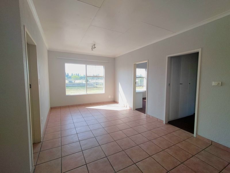 A bright, empty living room featuring neutral walls and tiled flooring, offering a clean canvas for personalization.