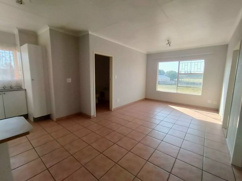 An open-plan living and kitchen area featuring ceramic tile flooring, security bars on windows, and neutral wall finishes in a vacant apartment setting.