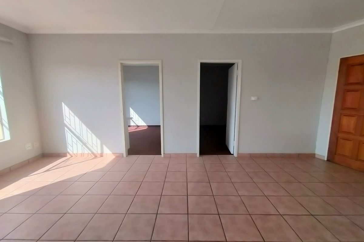 An empty living area featuring tiled flooring, a window with security bars, and access to adjacent rooms through two doorways.