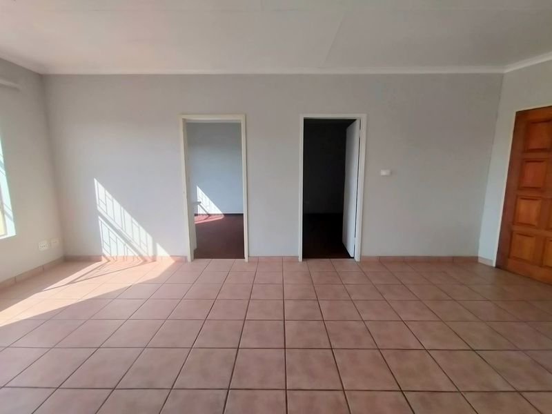 An empty living area featuring tiled flooring, a window with security bars, and access to adjacent rooms through two doorways.