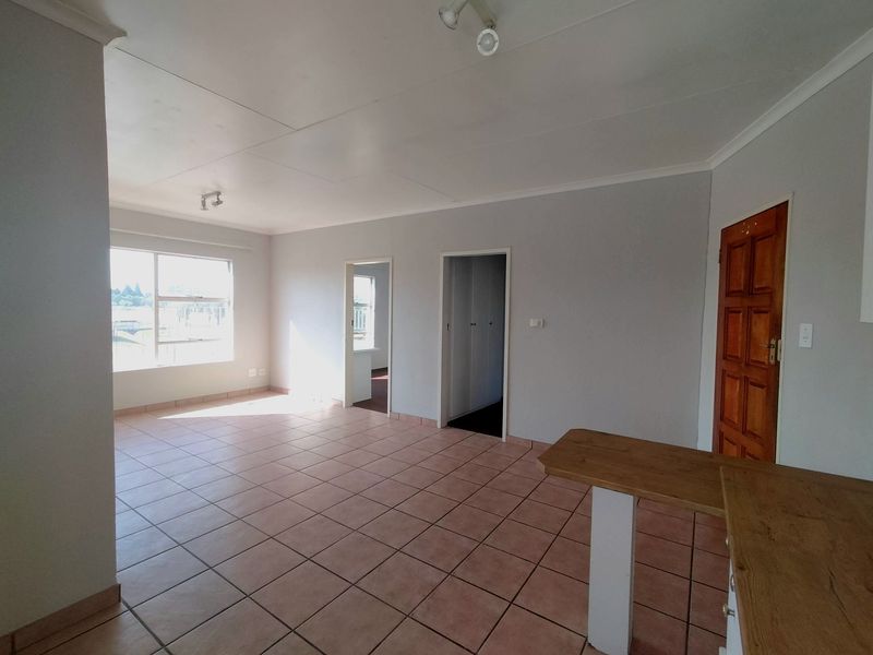Spacious open-plan living area featuring tiled flooring, a breakfast bar, and neutral wall finishes, offering a versatile layout for dining and relaxation.
