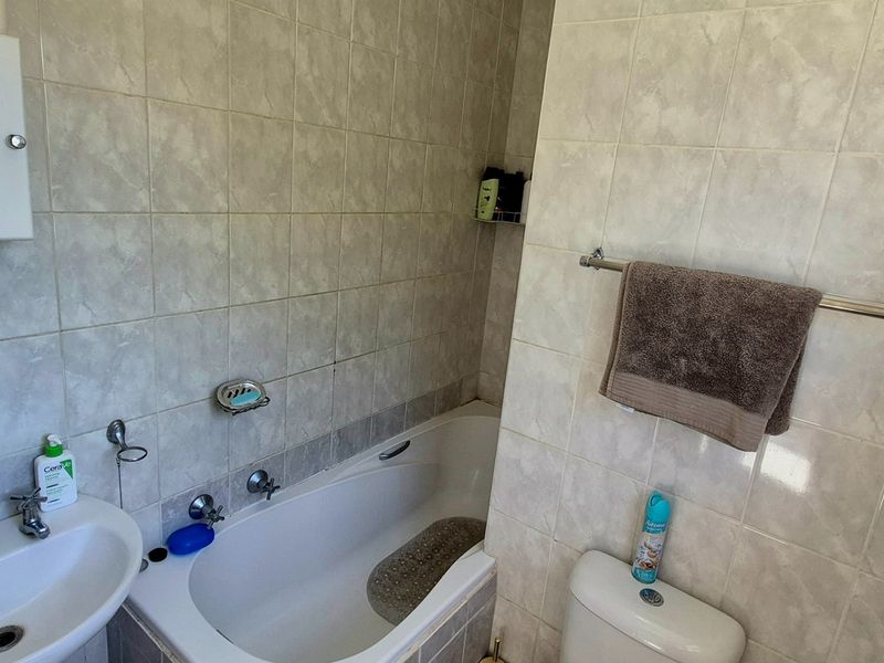 A functional bathroom featuring a bathtub, pedestal basin, toilet, and neutral wall tiling, offering a practical layout for daily use.