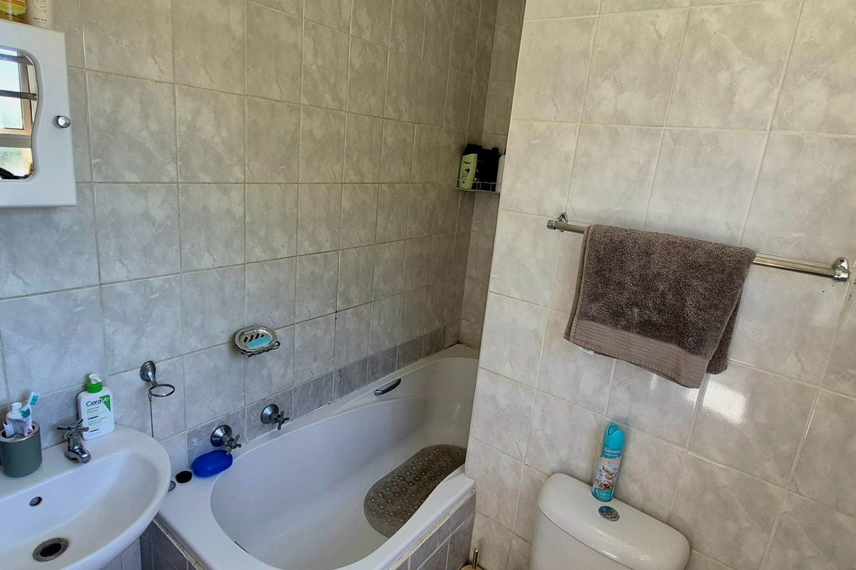 A functional bathroom featuring a bathtub, pedestal basin, toilet, and neutral wall tiling, offering a practical layout for daily use.
