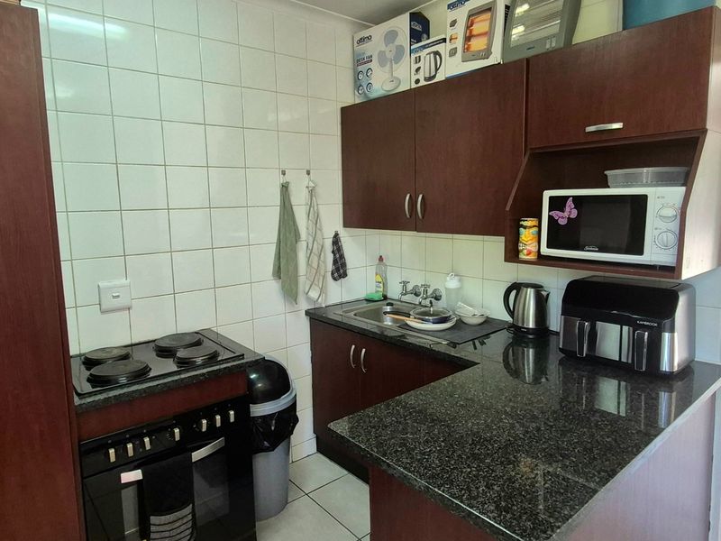 Compact kitchen featuring dark wood cabinetry, granite countertops, a built-in electric stove and oven, and tiled backsplash.