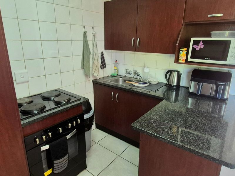Compact kitchen featuring dark wood cabinetry, granite countertops, tiled backsplash, and a built-in electric stove with oven.