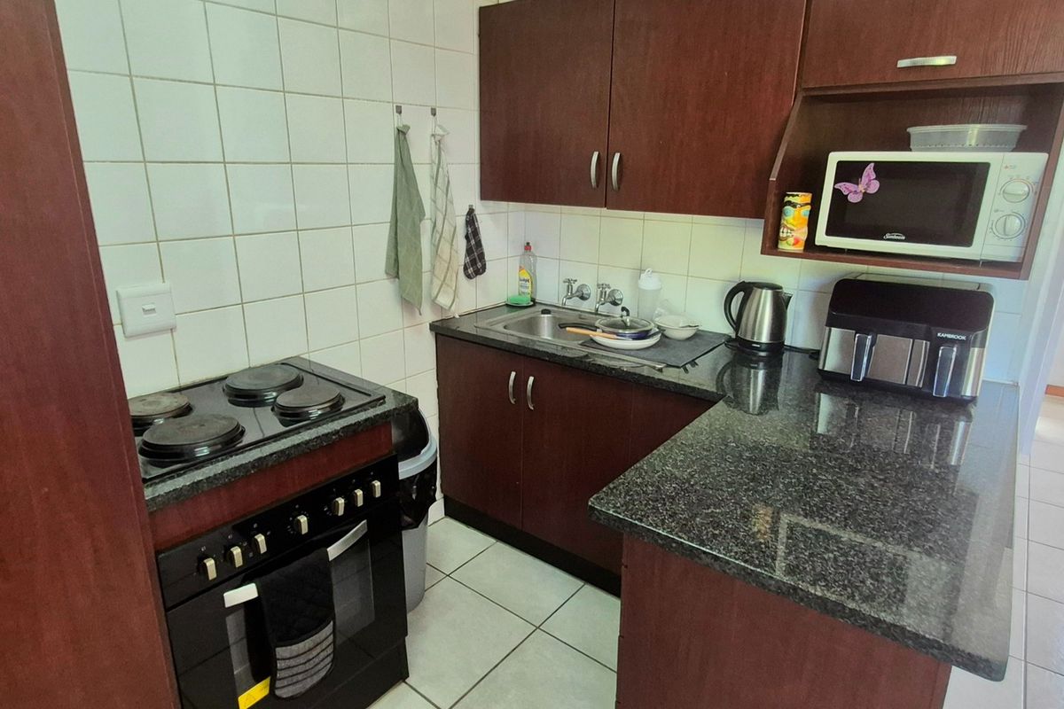 Compact kitchen featuring dark wood cabinetry, granite countertops, tiled backsplash, and a built-in electric stove with oven.