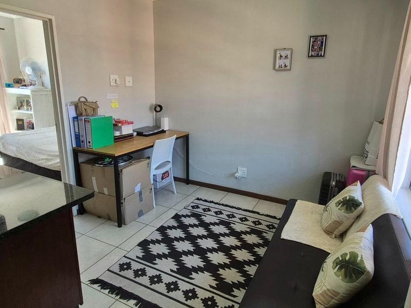 Open plan living area featuring tiled floors, a compact kitchen corner with granite countertops, and access to an adjacent bedroom space.