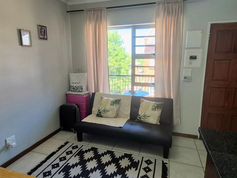 Open-plan living area featuring tiled flooring, a large window with natural light, and a solid wood entrance door.