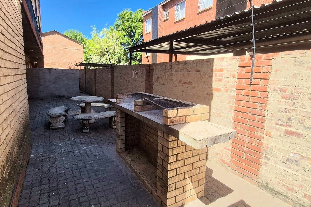 Outdoor rear courtyard area featuring a permanent brick-built braai, paved flooring, and secure perimeter walling with electric fencing.