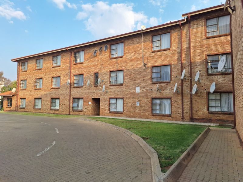 Exterior view of a multi-story brick apartment building featuring a paved driveway and multiple satellite dish installations on the facade.
